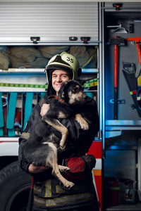 车站消防车背景下戴头盔带狗的年轻消防员照片