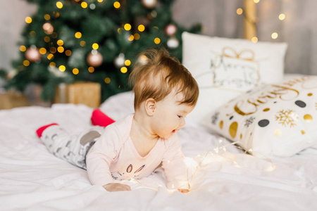 美丽的新生女孩坐在床上，带着花环在圣诞树的背景下微笑