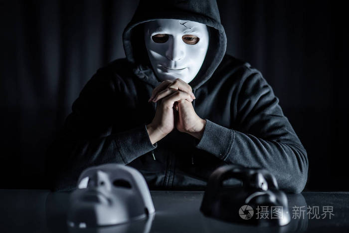 帽衫男戴着神秘面具,在桌子上选择黑色或白色面具. 匿名社交伪装.