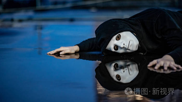 在雨后,神秘的帽衫男子在白色面具下感到沮丧和失望,躺在潮湿的地板上