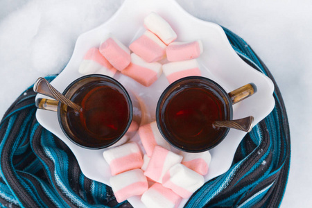 一棵树下有两杯棉花糖的茶，在冬天的雪地里裹着蓝色的围巾