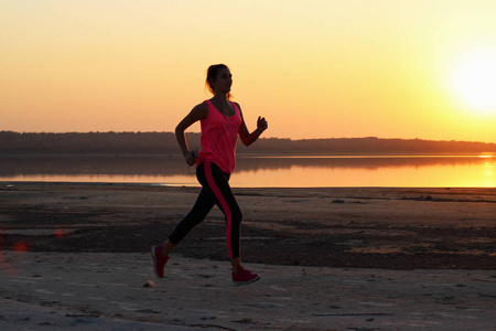 年轻漂亮的女人在橙色的夕阳背景下沿着海滨奔跑。