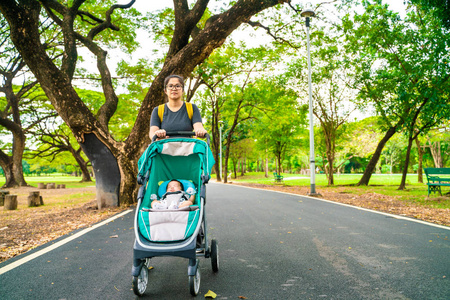 母亲带着婴儿游乐设施在绿色公园和婴儿车放松