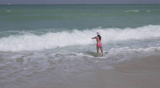 身穿游泳衣的少女在迪拜海滩上的波斯湾海浪中愉快地跳来跳去