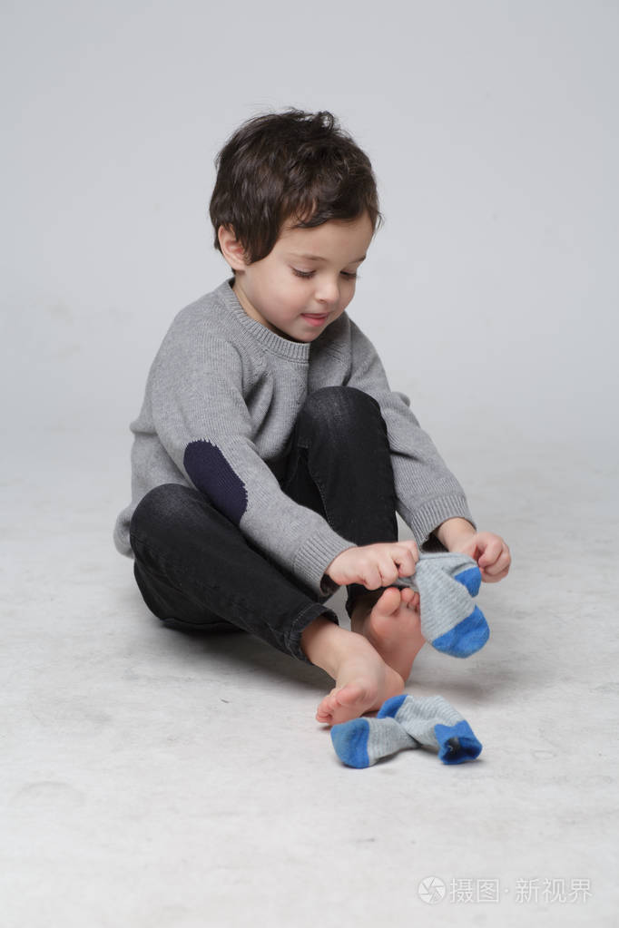 可爱的小男孩坐着的肖像,学习如何穿袜子由他自己快乐