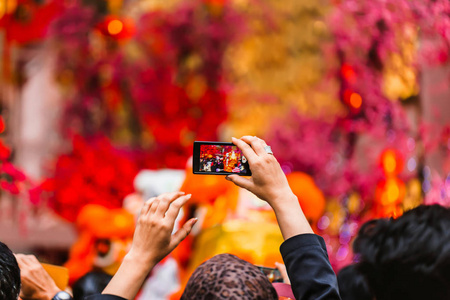 一个女人在她的电话表演艺术家上拍照。 中国新年。 红色背景。 美丽的波克。 假日灯