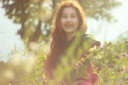 一个快乐的年轻白种人，留着长长的红色头发，手里拿着一束着一束花，放在一片充满鲜花和阳光的田野上。 明亮的春天