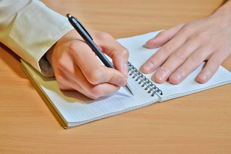 s hand in a white shirt writes the text with a black pen in a no