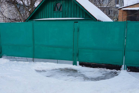 在白雪皑皑的乡村街道上，一扇绿色封闭的私人金属大门