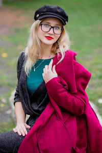 今年秋天，戴着眼镜和帽子的可爱年轻女人穿着一件红色外套在公园里散步。