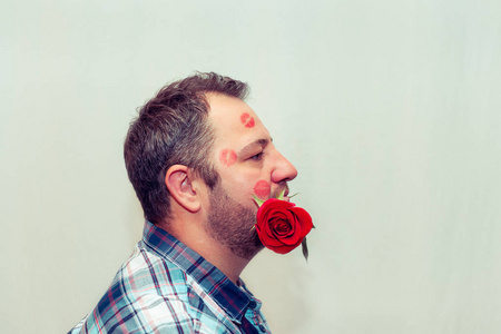 长胡子的成熟男人嘴里衔着一朵红玫瑰。 他脸上有口红的痕迹。