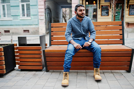 时尚的印度胡须模特男子穿休闲服装，户外坐在印度街的长凳上。