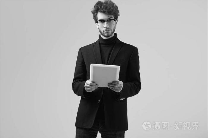 的男人,卷发,穿西装,戴眼镜,在工作室里戴着一块灰色背景的平板电脑