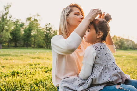 美丽的母亲做发型的肖像给她可爱的小女孩一起在公园里度过的时光。 快乐的女人和她可爱的孩子在公园里玩。 母亲节快乐。 母亲和儿童