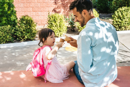 后景快乐可爱的小女孩坐在城市街道上和英俊的爸爸一起在户外吃冰淇淋。 有趣的女孩孩子和父亲在外面玩得很开心。 爸爸和女儿的良好关系
