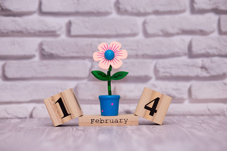 2月14日，每月14日在木制日历上，白色砖块背景上有玩具花。 情人节快乐。