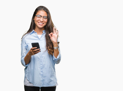年轻漂亮的阿拉伯女人用智能手机在孤立的背景下发短信，用手指做OK标志，优秀的符号