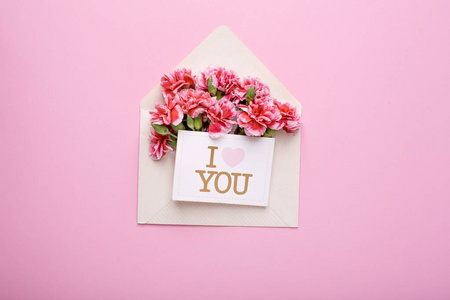 一个带有粉红色花的信封和一张我爱你的卡片，放在粉色背景的顶部