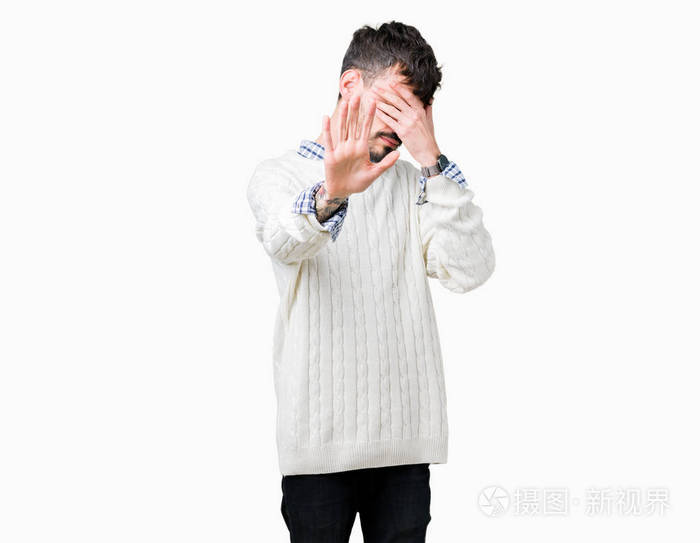 年轻的帅哥穿着冬天的毛衣在孤立的背景上用手遮住眼睛用悲伤和恐惧的