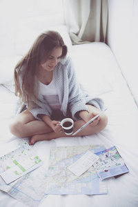 坐在床上的放松的年轻妇女与一杯咖啡和数字式片剂
