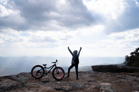 一个人站在岩石山上的自行车旁，眺望美丽的自然景色和美丽的蓝天