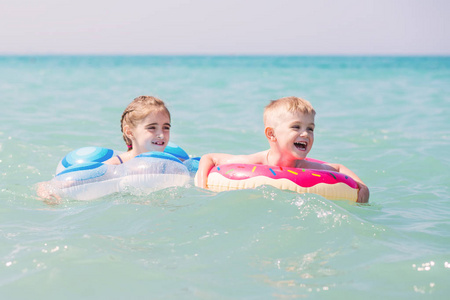 夏天，两个快乐的孩子在海里的充气圈上游泳