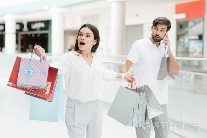 男人和女人正走到购物中心的另一家商店.男人在电话里聊天