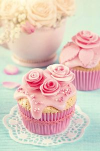 蓝色木制背景上有粉红色花朵的纸杯蛋糕
