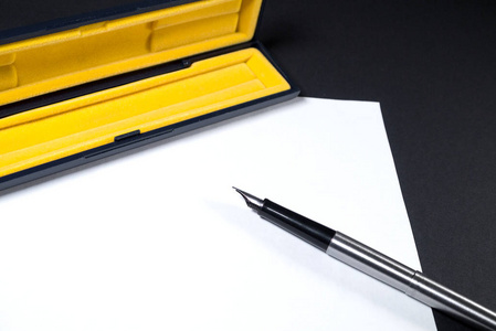 白纸上有一支钢笔和一个黄色的盖子。 黑色背景