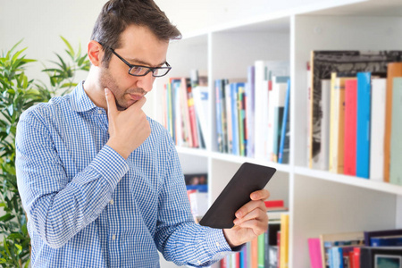 男人拿着电子书在书架背景和阅读。