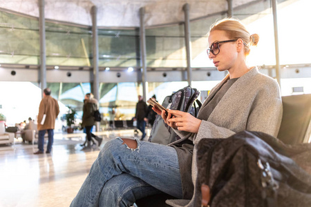 在机场航站楼登机口等候登机时, 女性旅行者在使用手机时使用手机