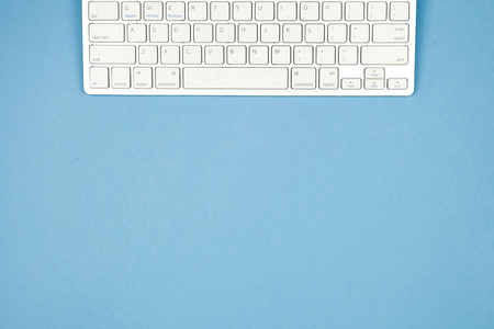 蓝色背景上的紧凑型白色无线键盘。 复制空间。