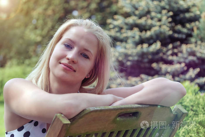 一张冷笑的金发女郎坐在花园的木椅上的特写照片.那个