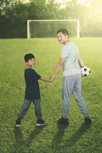 在足球场上，年轻的父亲带着一个球看着摄像机