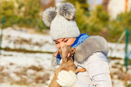 年轻的女人在外面雪地里玩得很开心。 雌性在寒冷的冬天和她的小纯种狗小狗玩耍。