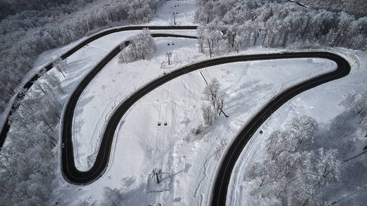 空中无人驾驶飞机看到一条弯曲的蜿蜒的道路，穿过森林，在冬天，山上覆盖着白雪