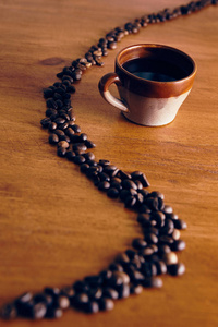 棕色的杯子站在木桌上，咖啡豆用一条曲线摆出来