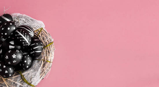 复活节背景，黑色鸡蛋和明亮的图案手工在干草巢粉红色背景