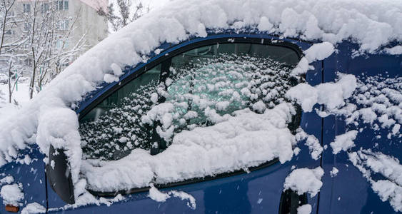 冰冻的汽车蓝色小货车在冬天覆盖了雪。 在暴风雪中冬季城市生活的城市场景。