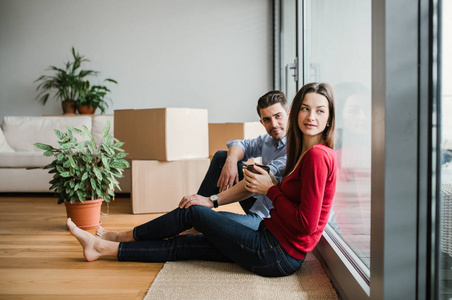年轻夫妇与纸板箱移动在一个新的家, 坐在地板上