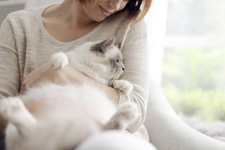 年轻快乐的女人坐在客厅的扶手椅上，抚摸美丽的猫