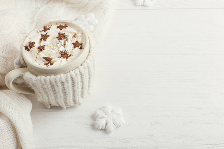 一杯热冬饮料，加鲜奶油和一个带有星号的白色雪花和木制桌子上的针织围巾的除尘粉。 明亮颜色的圣诞节概念。 复制空间。