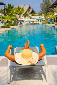 在豪华的热带度假胜地的游泳池里躺在日光浴床上放松的女人