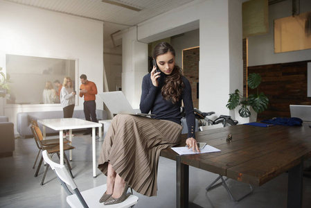 年轻女商人坐在办公室工作时用手机与某人交谈的完整镜头。