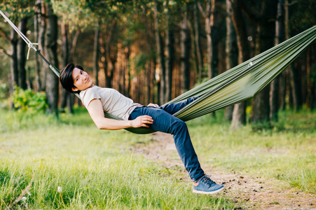 在阳光明媚的夏日，年轻人在森林的吊床上放松