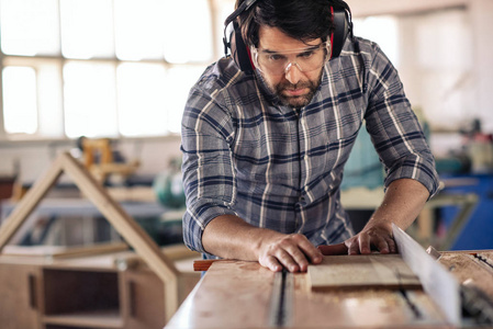 在木工工作室工作时，木匠用锯子用安全齿轮在木板上精确切割