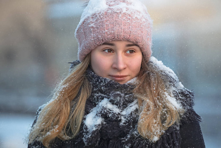 冬天在户外的美丽的年轻女孩，雪中的粉红色帽子和蓝色围巾，降雪