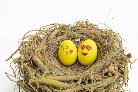 两个复活节彩蛋涂有表情符号，一个在爱情中，另一个在亲吻中，放置在一个孤立的白色背景下的巢中。