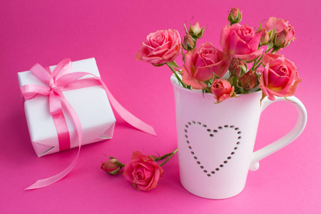 白色杯子里的粉红色玫瑰和深粉色背景上的粉红色蝴蝶结的礼物