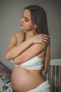 有吸引力的孕妇坐在床上, 抱着她的肚子。怀孕的最后几个月